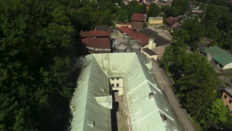 A-historic,-vintage-brewery-with-smoking-chimneys,-surrounded-by-green-trees-during-summer-in-Poland