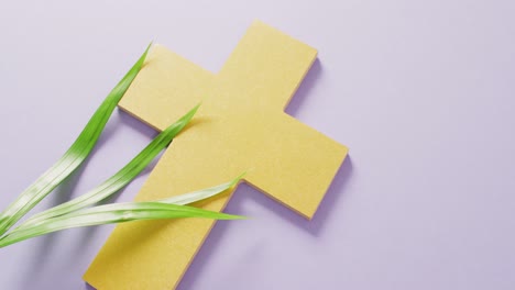 video of palm sunday palm leaves and yellow christian cross on lilac background with copy space