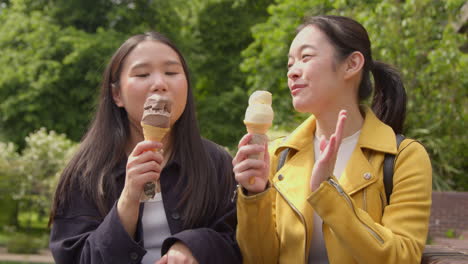 Two-Smiling-Young-Female-Friends-Meeting-And-Eating-Ice-Cream-Outdoors-In-Park-Together-3