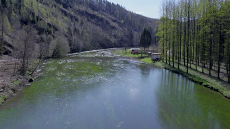 Volando-Rápido-Sobre-Un-Río-Ancho-En-Un-Terreno-Montañoso-Cubierto-De-Vegetación-Verde-Durante-El-Día