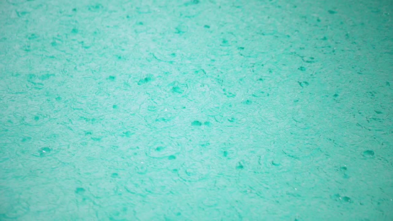 Slow motion top-down shot of rain drops hitting pool surface, creating turbulent surface and ripples