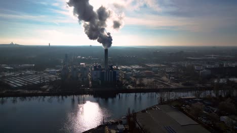 large industrial power plant emitting large amounts of smoke over the city berlin next to a river on a sunny day. lovely aerial view flight panorama overview drone