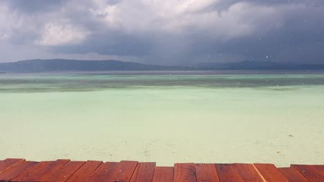 lluvia en el muelle de madera en los trópicos con vistas al agua turquesa del océano en la isla tropical de raja ampat, papúa occidental, indonesia