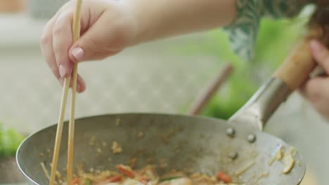 woman stirring hot wok noodles with chopsticks