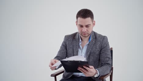 handsome man in grey costume holding a folder. young businessman sitting in the chair and reading documents. slow motion.