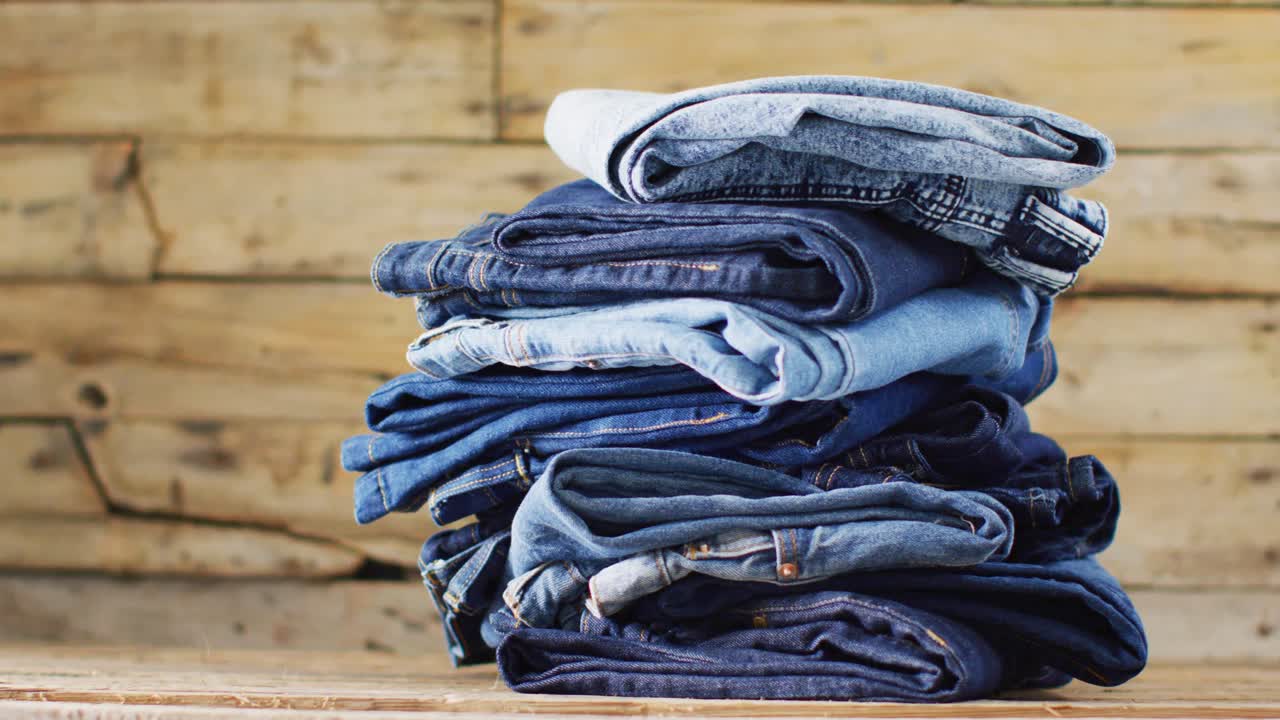 Close up of folded jeans with different shades on wooden background with copy space