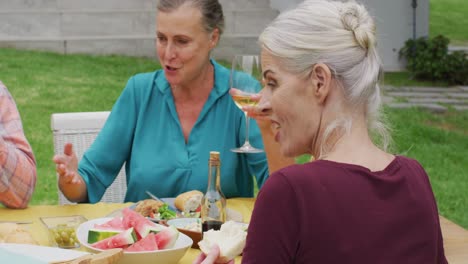 animation of happy caucasian senior woman eating lunch in garden with friends