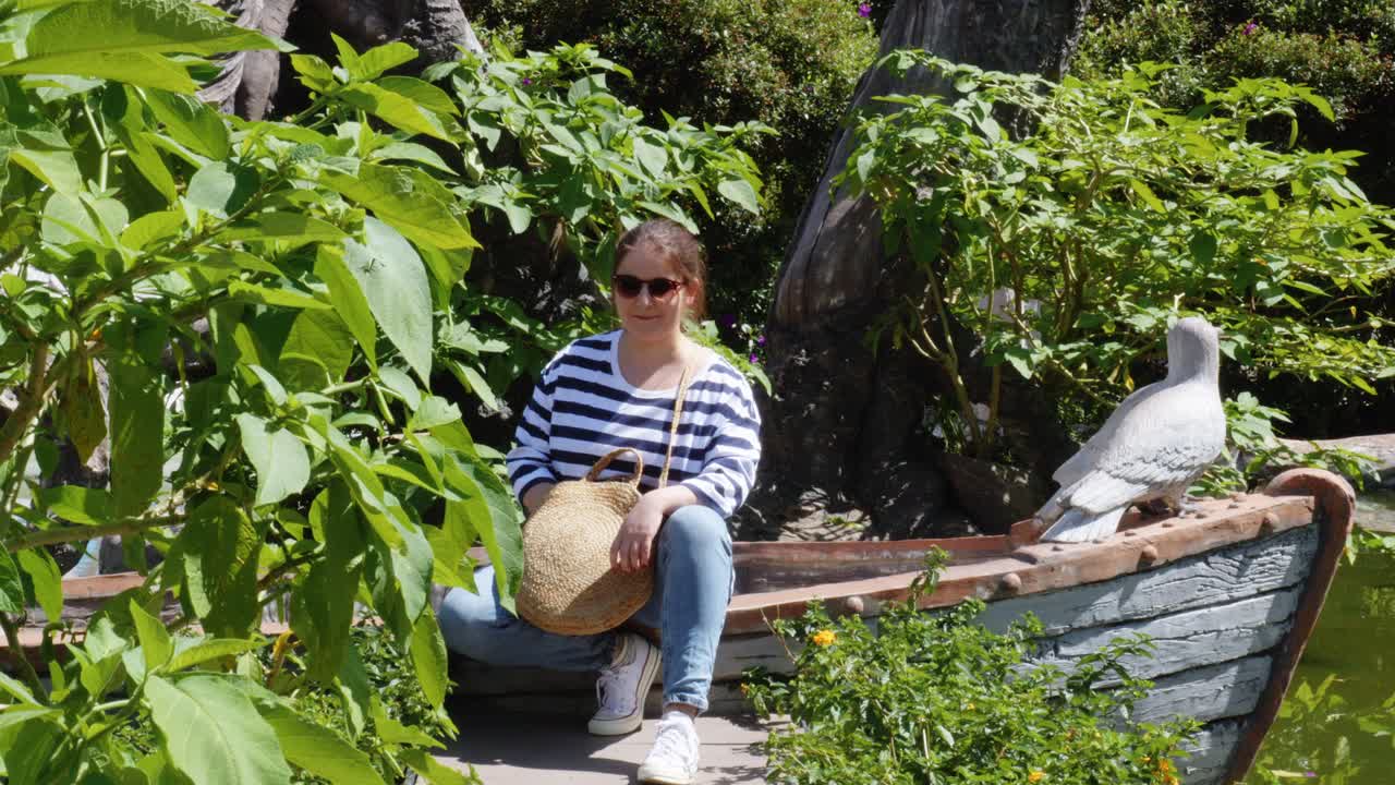 정적 샷은 베트남 달랏의 점토 터널에서 보트 모양의 점토 조각 옆에 앉아 있는 30대 여성을 포착합니다.