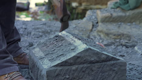 handheld shot showing a handheld pick being used by a craftsman to shape a block of stone from the city of ancud, chiloe island