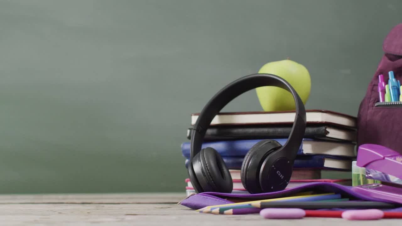 Video of school supplies and books on wooden table over blackboard