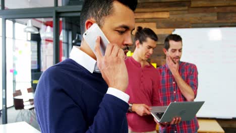 Business-executive-talking-on-mobile-phone-while-colleague-working-in-background
