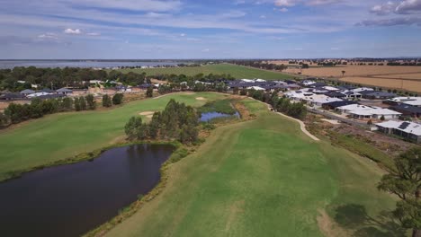 Vista-Aérea-Baja-Sobre-Un-Campo-De-Golf-Y-Obstáculos-De-Agua-Y-Mirando-Más-Allá-De-Los-Campos-Agrícolas-Y-El-Lago-Mulwala