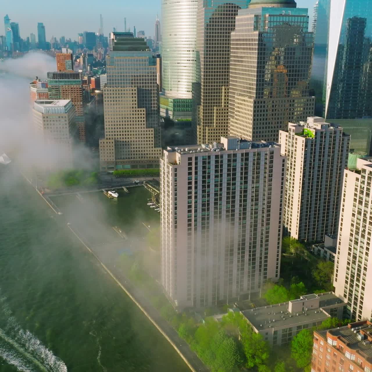 Manhattan Island skyscrapers reflecting morning sun. Flying over the East river waterfront covered with light smoke fog