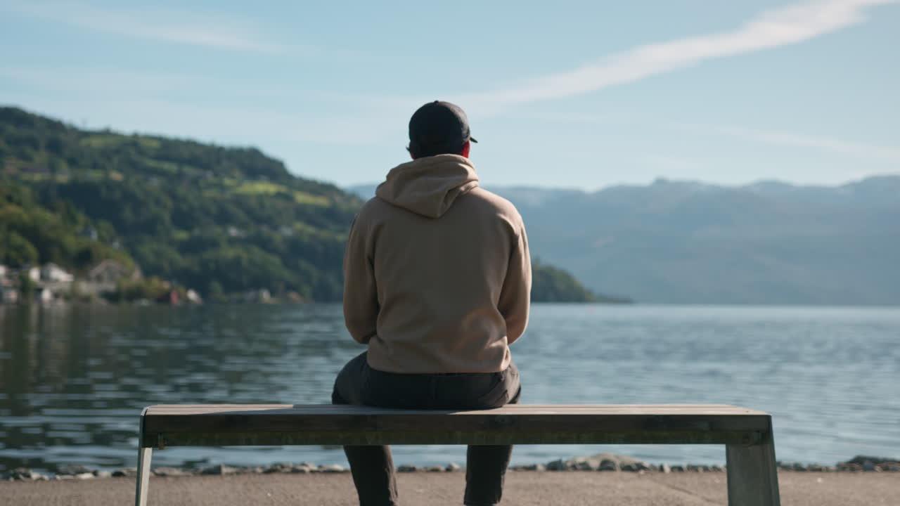 Man sitting alone on a bench on a sunny day looking out to the hardangerfjord in Norway