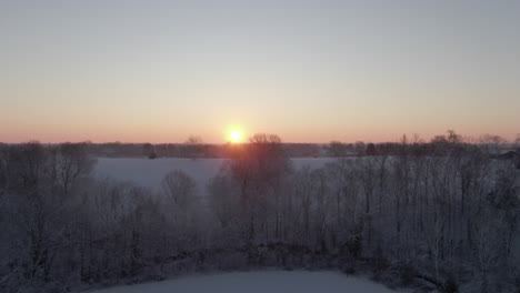 rise over snow-covered trees and field to reveal the sunrise on the horizon