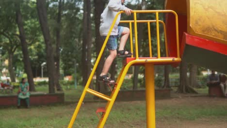 niño feliz escalando un gran tobogán rojo anaranjado