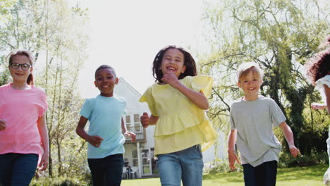 Gruppe-Von-Kindern,-Die-Zu-Hause-über-Den-Gartenrasen-Laufen-Und-In-Die-Kamera-Schauen