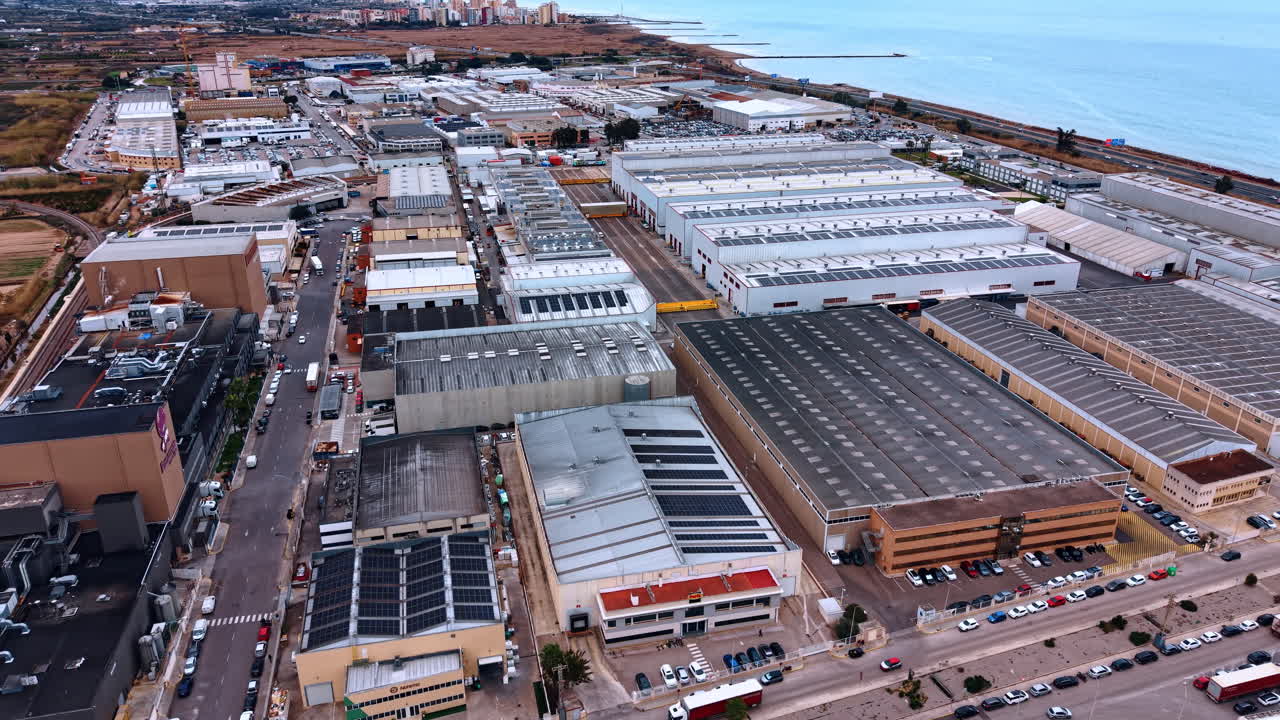 Madrid, Spain, 8 August 2025: High angle view of industrial warehouses near the sea. Aerial perspective of an industrial zone with logistics buildings, parking lots, and a coastal highway by the ocean