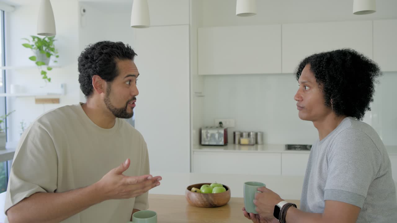 African American men chatting at island, responding as right man starting speaking, sipping mugs