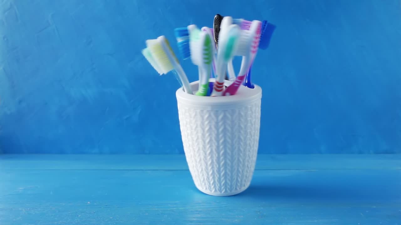 muchos cepillos de dientes diferentes en una taza blanca giran en una mesa contra un fondo azul. video de bucle crudo creativo 4k con efecto de rampa de velocidad. filmado en cámara de cine de alta velocidad, 1000 fps.