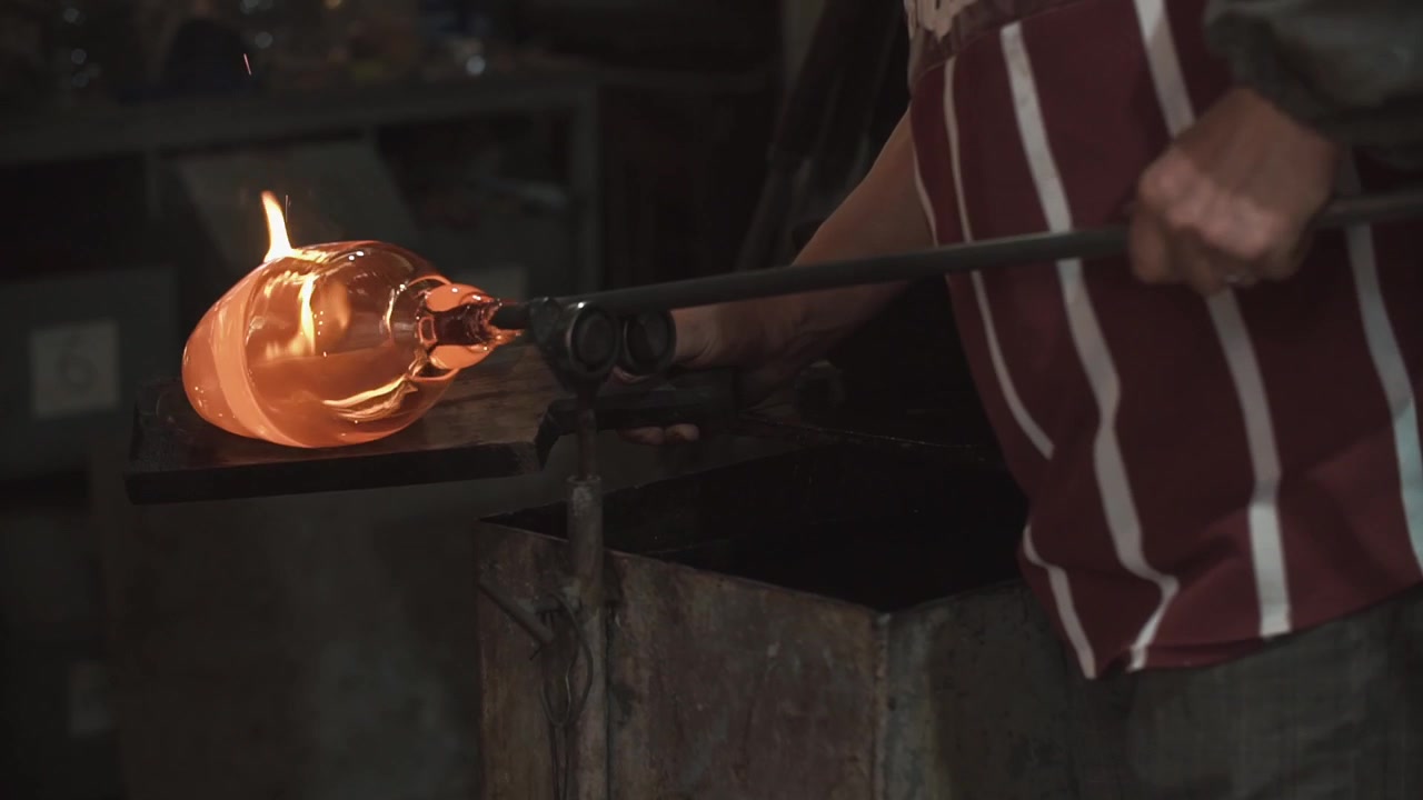 Glassblower Shaping Molten Glass with a Blowpipe in a Dark Workshop