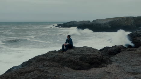 a man contemplates the stormy ocean from a rocky coast