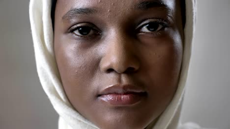 face ofoung sad african muslim girl in hijab is looks up and watching at camera, religioun concept, grey background