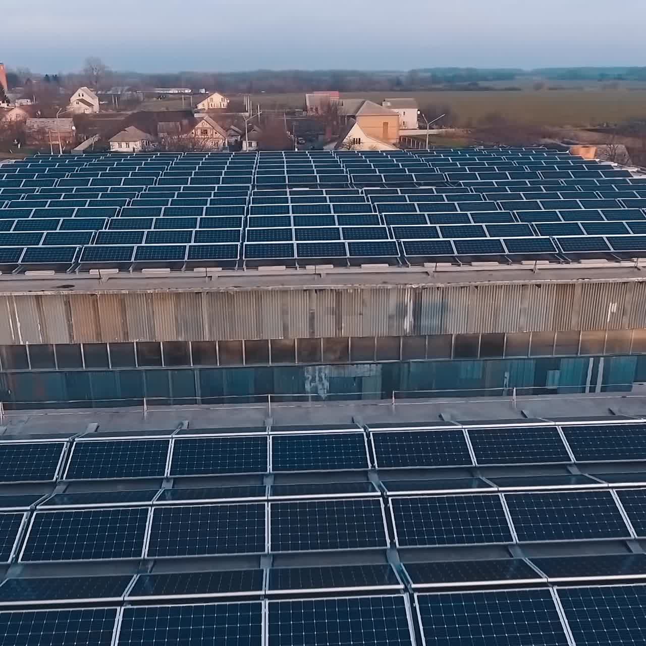 Solar energy farm on the roofs at sunset. Many solar panels on roofs of buildings in the countryside. Motion camera back. Aerial view.