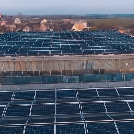 solar energy farm on the roofs at sunset. many solar panels on roofs of buildings in the countryside. motion camera back. aerial view.