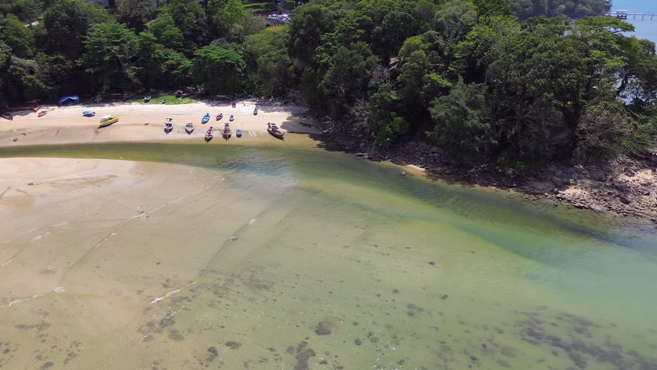 Flying backwards and turning left, revealing scenic Patong Beach, parked Thai taxi boats, a coastal bridge, and the lively Phuket shoreline.