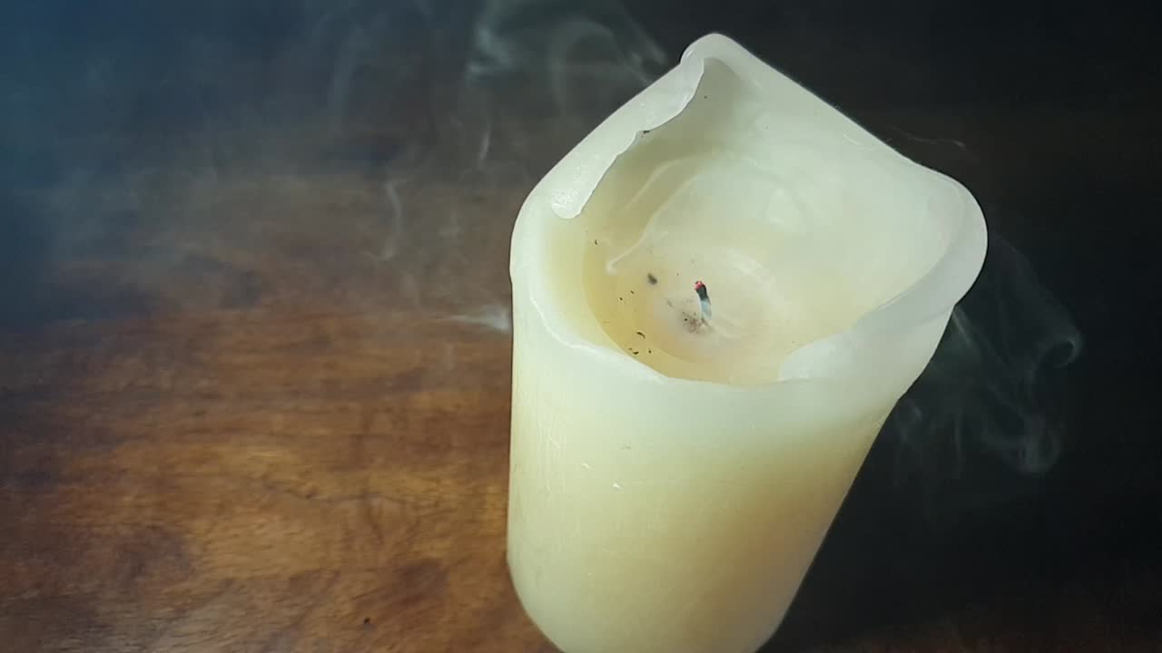 haunted theme and scary white smoke fog rolling over an old oak table with a dark background over and past a burning candle flame