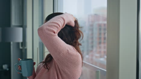 relaxed housewife looking panoramic window holding coffee cup at home closeup