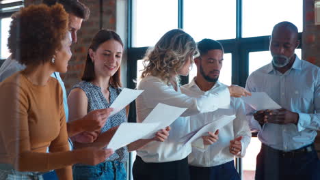 mujer de negocios que lidera una reunión de equipo en una oficina multicultural ocupada entregando documentos