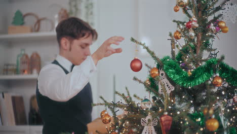 hombre guapo colgando joyas rojas en el árbol de navidad en casa
