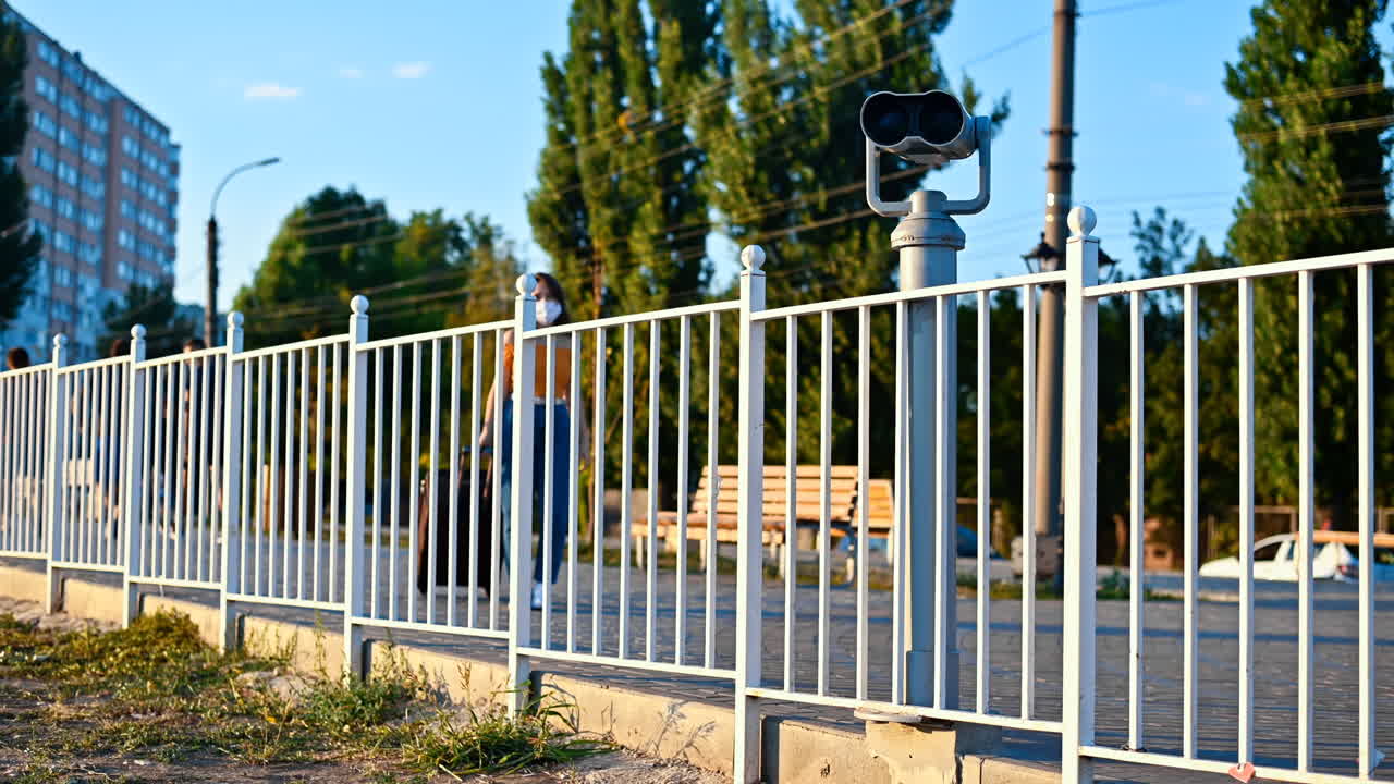 Young woman in protective medical mask looking into a tower viewer from the observation deck at the city at sunset. Corona Virus idea. Safe travel during the pandemic. Slow motion. Chisinau, Moldova