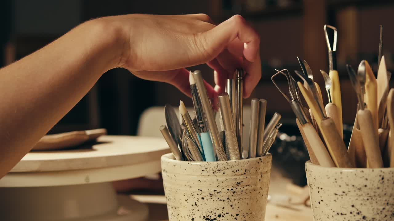 Hand reaching for pottery sculpting tools in an artist's studio