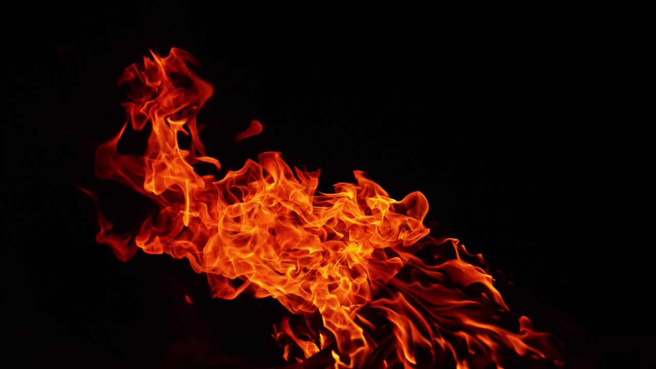 Flame of bonfire bending to the side. Wooden logs burn well at night. Smoke creeping by the ground.