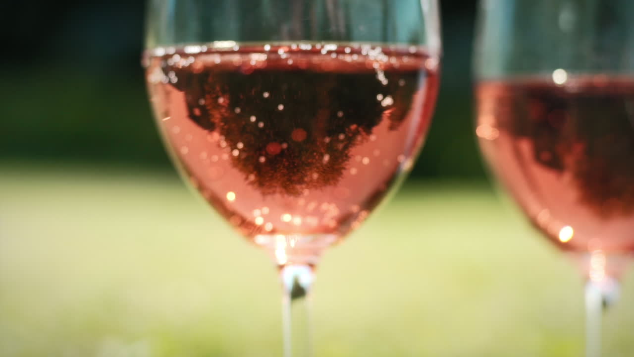 Ros&eacute; Wine Glasses Sparkling against a Green Background in Slow Motion