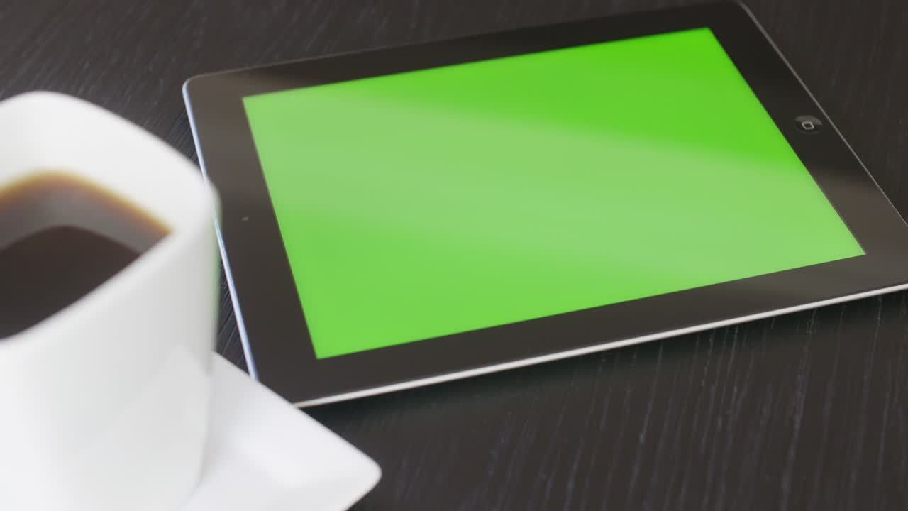 tableta se mueve a la derecha de detrás de la taza de café en la mesa con verde
