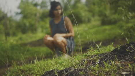 Beautiful-young-woman-in-sundress-squats-on-hillside-pondering-life,-slow-motion-rack-focus