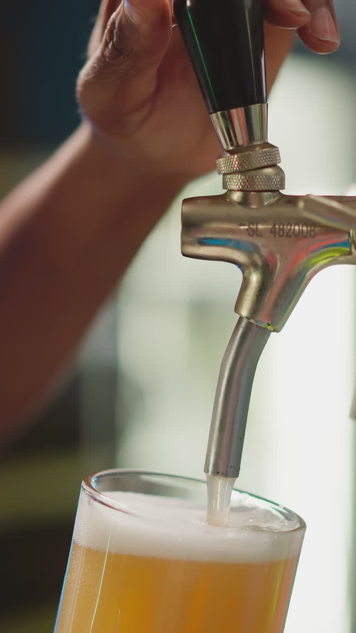 el camarero vierte cerveza en un vaso en un pub de primer plano. el camarero afroamericano llena la taza con cerveza fresca espumosa de la bomba en el mostrador. el hombre negro trabaja en el mostrado
