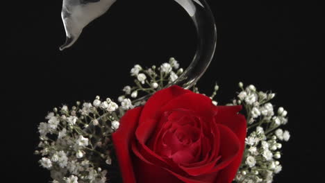 a red rose in a swan shaped vase surrounded with babies breath