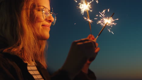 Frau-Hält-Wunderkerzen-Am-Strand-Bei-Sonnenuntergang-Und-Genießt-Die-Silvesterfeier.-Winkt-Spielerisch-Mit-Wunderkerzen-Und-Feuerwerk.-Mädchen-Feiert-Den-Unabhängigkeitstag-Am-4.-Juli