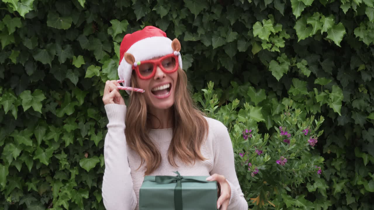At Christmas, Smiling woman in Santa hat holding gift and candy cane outdoors