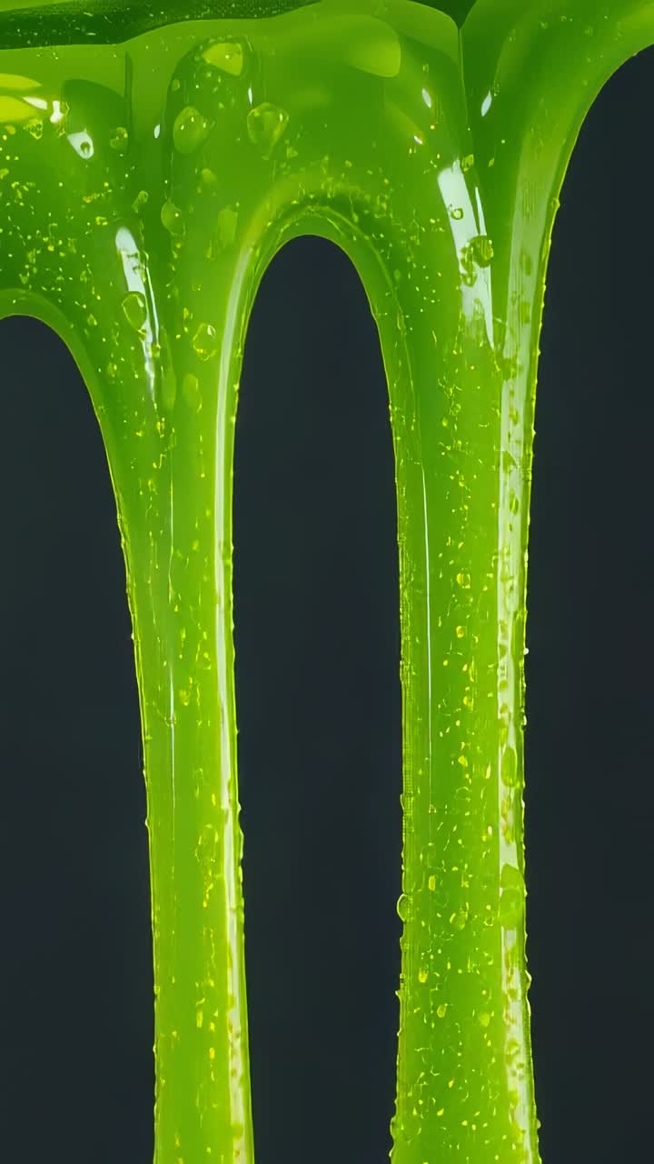 Vertical video: Dripping neon green slime streams stretching by gravity in studio, with air bubbles