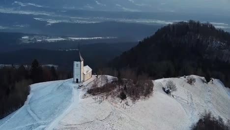 Vista-De-La-Iglesia-Jamnik-En-Un-Paisaje-Invernal-Con-Un-Colorido-Amanecer-En-Kranj,-Eslovenia