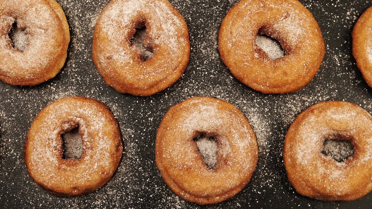 vista de arriba: toma de muñecas de una fila de rosquillas con azúcar en polvo en el escritorio negro