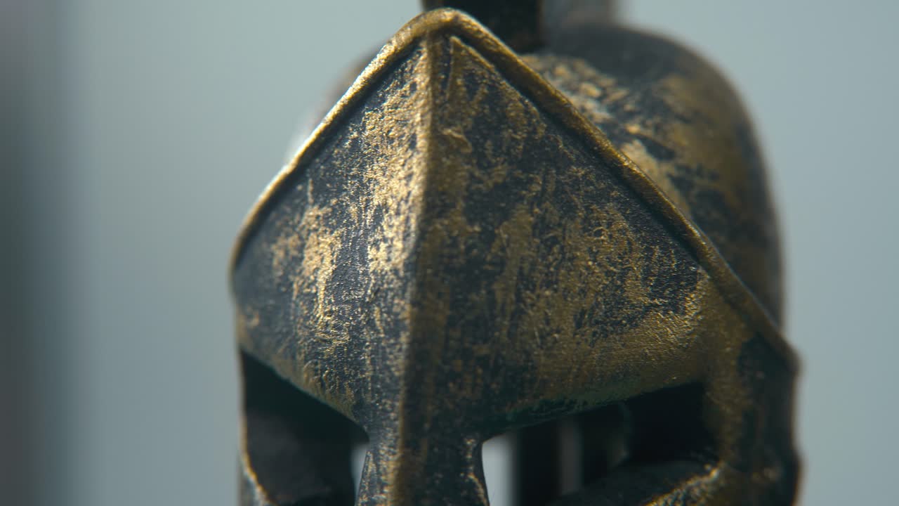 A close-up macro detailed shot of a Spartan design, two different ancient warrior metal bronze top of the helmets, glowing textured shapes, studio lighting, 4K cinematic video, Slow Motion, pan right