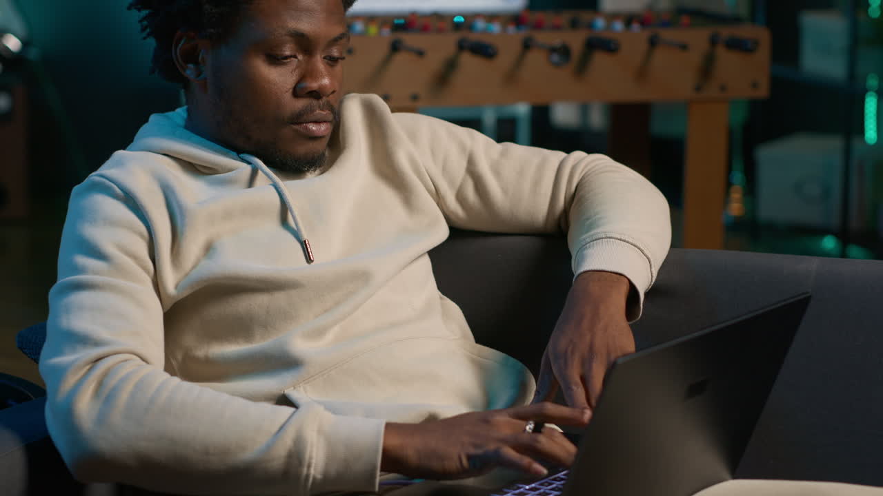 Smiling male freelancer browsing the web on laptop in a modern apartment, demonstrating a lifestyle of independence. Productivity in a virtual workspace, man multitasking. Camera A.