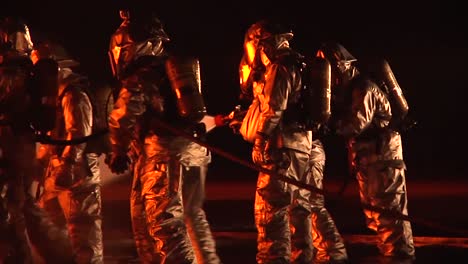 firemen in hazmat or heat resistant suits fight an intense fire at night 1